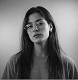 Black and white portrait of a young woman with long dark hair, looking slightly downward with a calm, thoughtful expression, soft lighting.